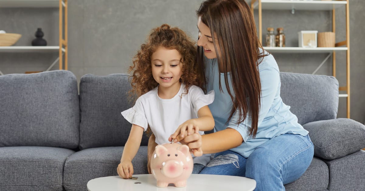 A mother and daughter discuss investing while the daughter adds money to a piggy bank.